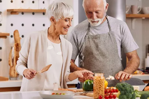 Glückliche und gesunde Senioren bereiten Essen zuhause zu